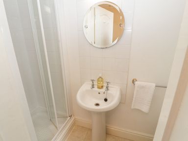 A small bathroom with a shower, pedestal sink with soap, round mirror, and towel rack with white towel at White House in Keswick