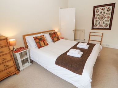 A bedroom with a double bed with white linens and two patterned pillows two bedside tables with lamps a wooden chest of drawers a decorative wall hanging a towel rack and folded towels on the bed at White House in Keswick