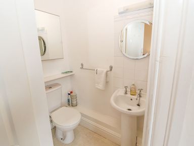 A small bathroom with a toilet and pedestal sink a round mirror above the sink and a towel rack with a towel at White House in Keswick