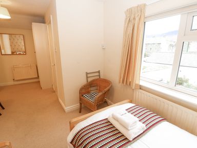 A bedroom with a single bed covered with a striped blanket and folded towels beside a window with curtains a wicker chair and a radiator at White House in Keswick