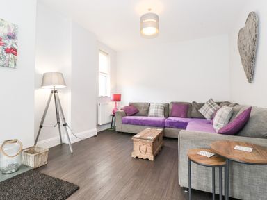A living room with a grey sectional sofa with purple cushions a wooden coffee table and two side tables at Latrigg House in Keswick