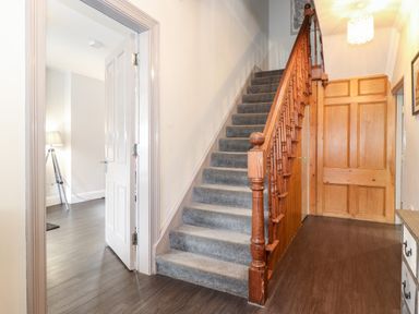 A hallway with carpeted stairs and wooden banister next to an open white door leading to a room with a tripod lamp at Latrigg House in Keswick