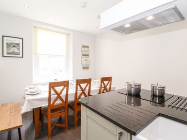 A dining area with a table set for six and a kitchen counter with two pots on a stove at Latrigg House in Keswick