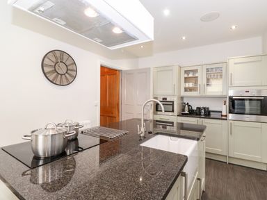 A kitchen with a black countertop island with a sink and pots a stove oven cabinets and a wall clock at Latrigg House in Keswick