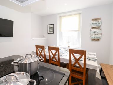 A dining area with wooden chairs around a table set for a meal and pots on a kitchen island at Latrigg House in Keswick