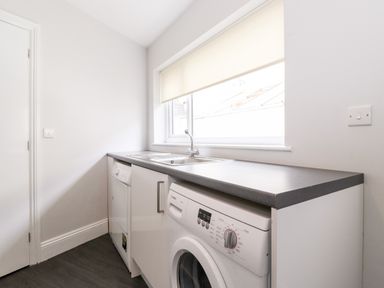 A laundry room with a washing machine a dishwasher a sink and a window with a roller blind at Latrigg House Keswick