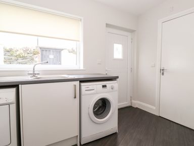 A utility room with a washing machine, sink, cabinet, window, and door at Latrigg House in Keswick