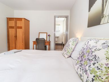 A bedroom with a bed and floral pillows a wooden wardrobe a desk with a chair and a mirror and an open door to a bathroom at Latrigg House in Keswick