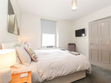 A bedroom with a bed a bedside table lamp a window with blinds and a wall-mounted television at Latrigg House in Keswick