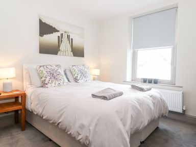 A bedroom with a double bed and floral pillows two bedside tables with lamps a window with a blind and artwork above the bed at Latrigg House in Keswick