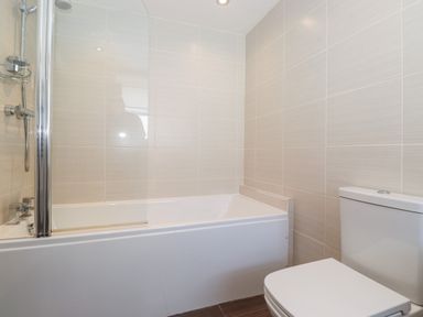 A bathroom with a bathtub that has a shower screen and a toilet at Latrigg House in Keswick