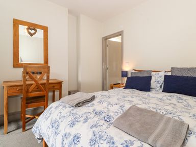 A bedroom with a bed with patterned bedding two folded towels a wooden desk and chair and a mirror at Latrigg House in Keswick