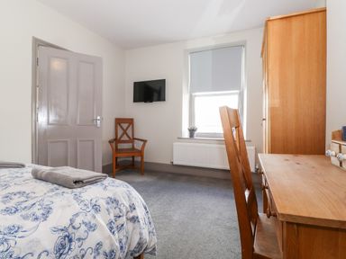 A bedroom with a bed covered in floral bedding a wooden chair a desk a wardrobe a window with a blind and a wall-mounted tv at Latrigg House in Keswick
