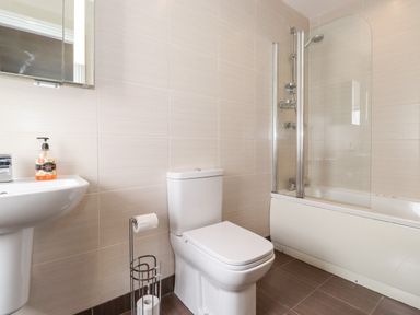 A bathroom with a white toilet a sink with a soap dispenser a bathtub with a glass shower screen and a toilet paper holder at Latrigg House in Keswick