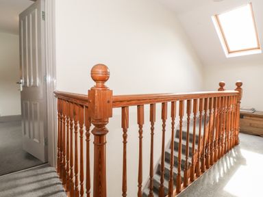 A stairway with wooden banister and gray carpet near an open door and skylight window at Latrigg House in Keswick