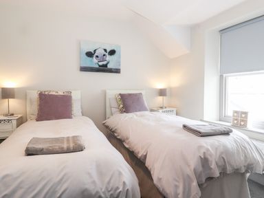 A bedroom with two single beds each with a folded towel on top two bedside tables with lamps and a window with a roller blind Latrigg House Keswick