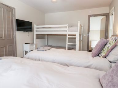 A bedroom with white bunk beds twin beds a wall mounted tv and a door leading to a bathroom at Latrigg House in Keswick