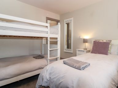 A bedroom with a bunk bed and a single bed with a nightstand and a wall mirror at Latrigg House Keswick
