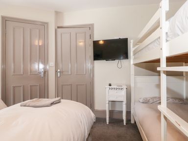 A bedroom with a white single bed with folded towels a white bunk bed a small white nightstand and a wall mounted television at Latrigg House in Keswick