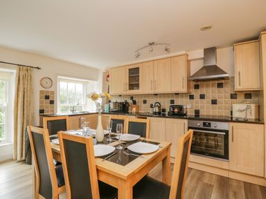 A kitchen and dining area with wooden cabinets a dining table with six chairs and place settings at Derwentwater Apartment in Keswick