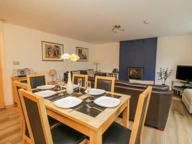 A dining area with a table set for six and a living room with brown sofas and a fireplace at Derwentwater Apartment in Keswick