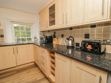 A kitchen with wooden cabinets black countertop a kettle toaster microwave and a window at Derwentwater Apartment Keswick