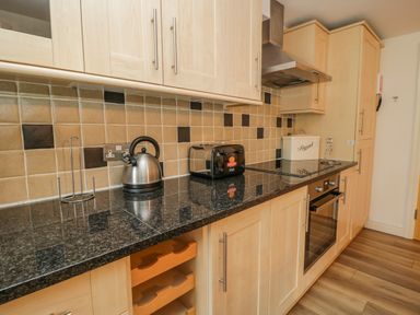 A kitchen countertop with a kettle, toaster, bread box, stove, oven, and wooden cabinets at Derwentwater Apartment in Keswick
