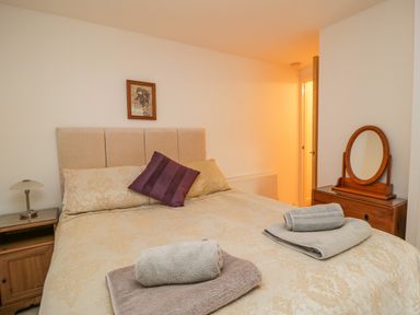 A bedroom with a bed arranged with towels a bedside table with a lamp and a wooden dresser with a round mirror at Derwentwater Apartment Keswick