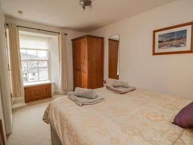 A bedroom with a bed towels on a bed a wooden wardrobe a wooden chest under a window and a framed picture on the wall at Derwentwater Apartment Keswick
