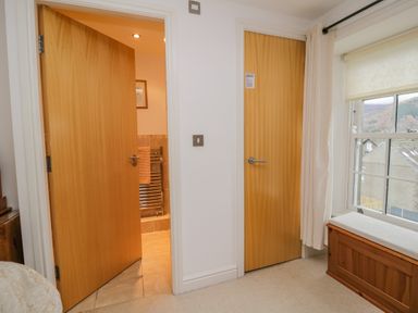 Two wooden doors in a room with a window and a wooden bench beneath the window at Derwentwater Apartment in Keswick