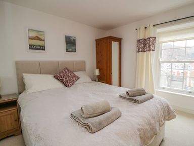 A bedroom with a large bed folded towels on it wooden furniture and a window with curtains at Derwentwater Apartment Keswick