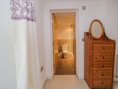 A wooden dresser with an oval mirror beside a doorway leading to a bathroom with a toilet and tiled floor at Derwentwater Apartment Keswick