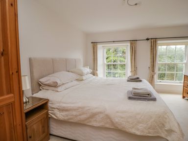 A bedroom with a large bed beside two windows with curtains at Derwentwater Apartment in Keswick