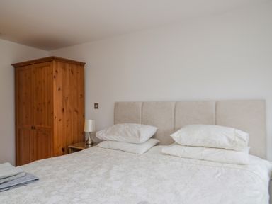 A bedroom with a double bed with pillows and a wooden wardrobe in the corner at Derwentwater Apartment in Keswick