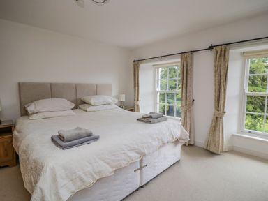 A bedroom with a large bed two bedside tables and windows with curtains at Derwentwater Apartment Keswick