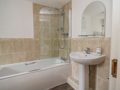 A bathroom with a bathtub, shower, sink, and mirror at Derwentwater Apartment Keswick