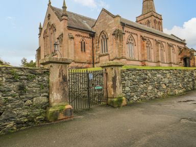 A stone church building with arched windows behind a stone wall and metal gate