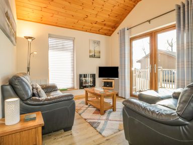 A living room with black leather sofas wooden coffee table TV and glass door at Holmedell in Greystoke