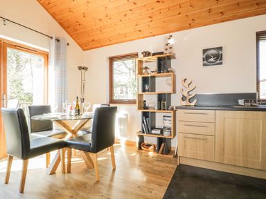 Dining area with a round glass table and four black chairs next to wooden shelves and a kitchen counter at Holmedell in Greystoke