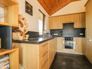 A kitchen with wooden cabinets black countertops a built in oven a sink a window and a wooden wine rack at Holmedell in Greystoke