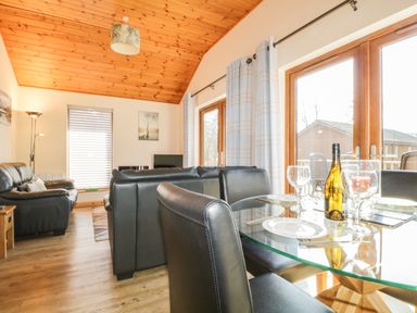 A living room with leather sofas a glass dining table set with plates glasses and a wine bottle at Holmedell in Greystoke