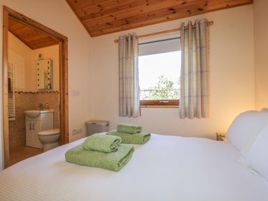 A bedroom with a bed with green towels on it a window with curtains and an ensuite bathroom at Holmedell in Greystoke