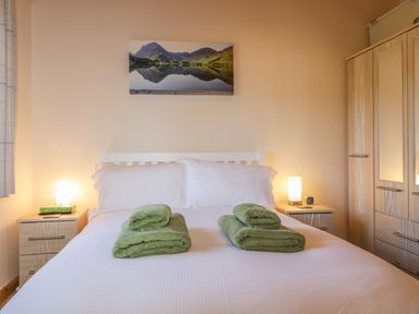 A bedroom with a double bed with green towels on it two bedside tables with lamps and a wardrobe at Holmedell in Greystoke