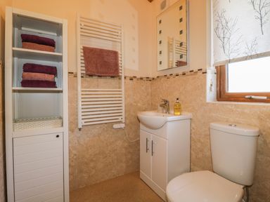 A bathroom with a white cabinet holding folded towels a white towel radiator a sink with a mirror above and a toilet next to a window at Holmedell in Greystoke