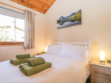 A bedroom with a white bed with green towels on it a window with curtains a wooden ceiling and bedside tables with lamps at Holmedell in Greystoke