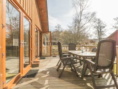 An outdoor wooden deck with a dining table and chairs outside a wooden building at Holmedell in Greystoke