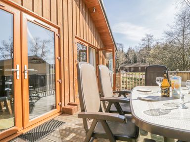 A wooden deck with a table set with plates drinks and glasses and outdoor chairs at Holmedell in Greystoke
