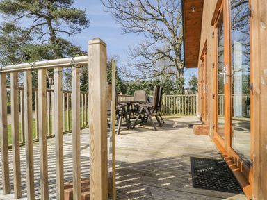 A wooden deck with railing and outdoor chairs next to a building with glass doors at Holmedell in Greystoke