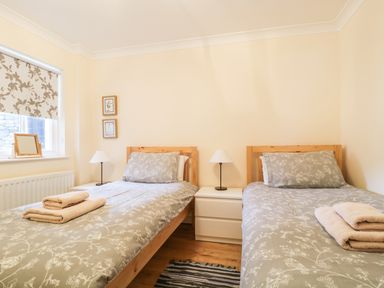 A bedroom with two single beds with grey floral bedding and towels on them at Siskin in Keswick