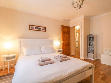 A bedroom with a double bed white bedside tables lamps an open wooden door and a white bookshelf at Siskin in Keswick
